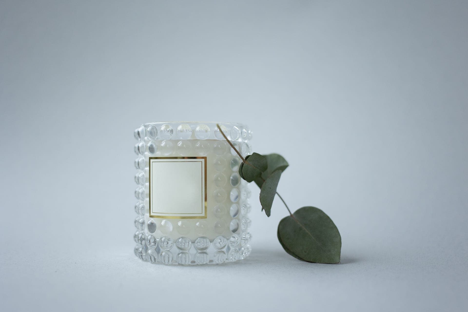 A eucalyptus sprig beside a matte ceramic bottle on porcelain